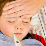 child with thermometer in mouth and person touching their forehead