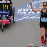 Dr. Tara Parks with arms up crossing finish line at Boston Marathon