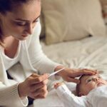 Mother touching infant's forehead while looking at thermometer
