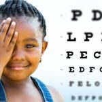 child covering one eye with hand with eye chart in background