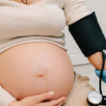 pregnant woman holding stomach while getting blood pressure taken