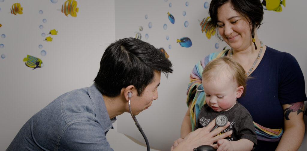 Doctor listening with stethoscope to infant on mother's lap