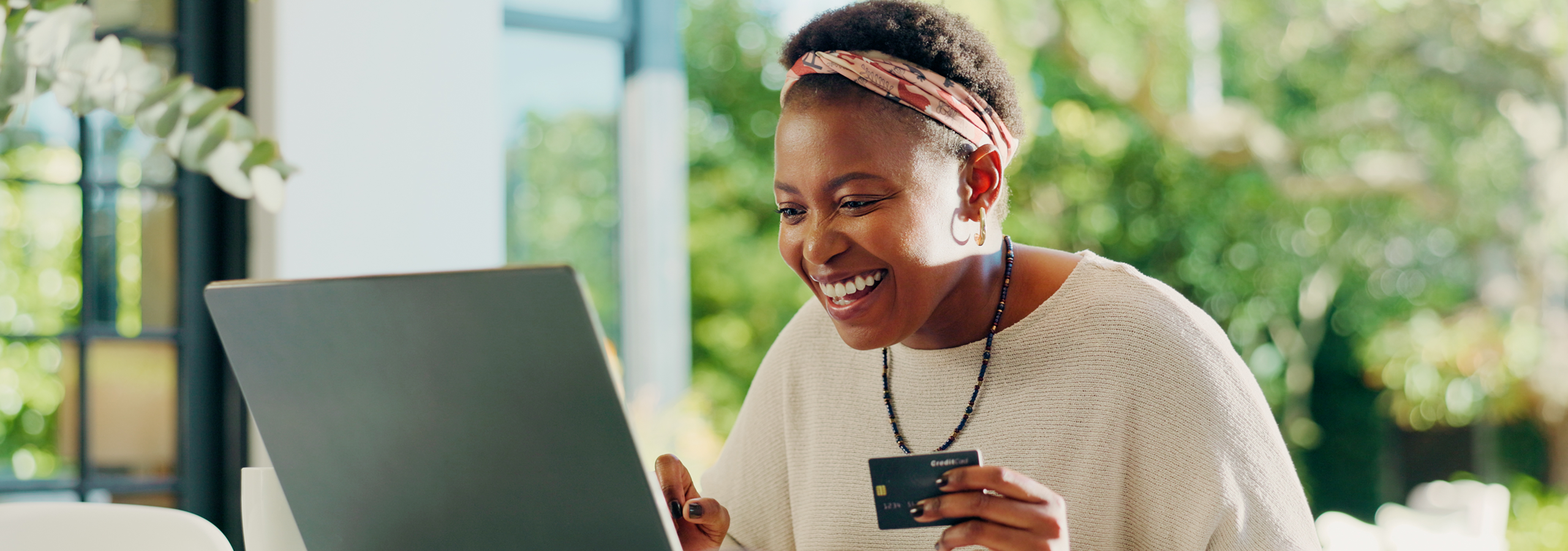 Woman smiling looking at computer with credit card in hand.