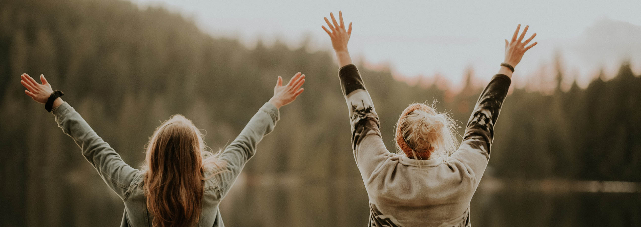 Two women with arms up looking out at pond